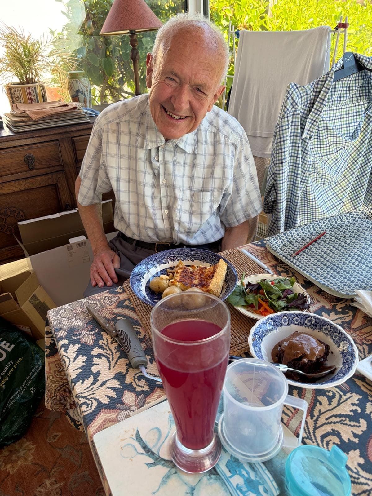 A customer at home smiling behind a delivered two-course meal of quiche, new potatoes and salad with a chocolate pudding