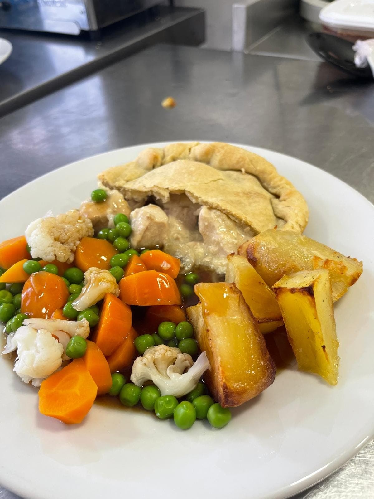 A plated chicken and mushroom pie with roast potatoes and fresh vegetables