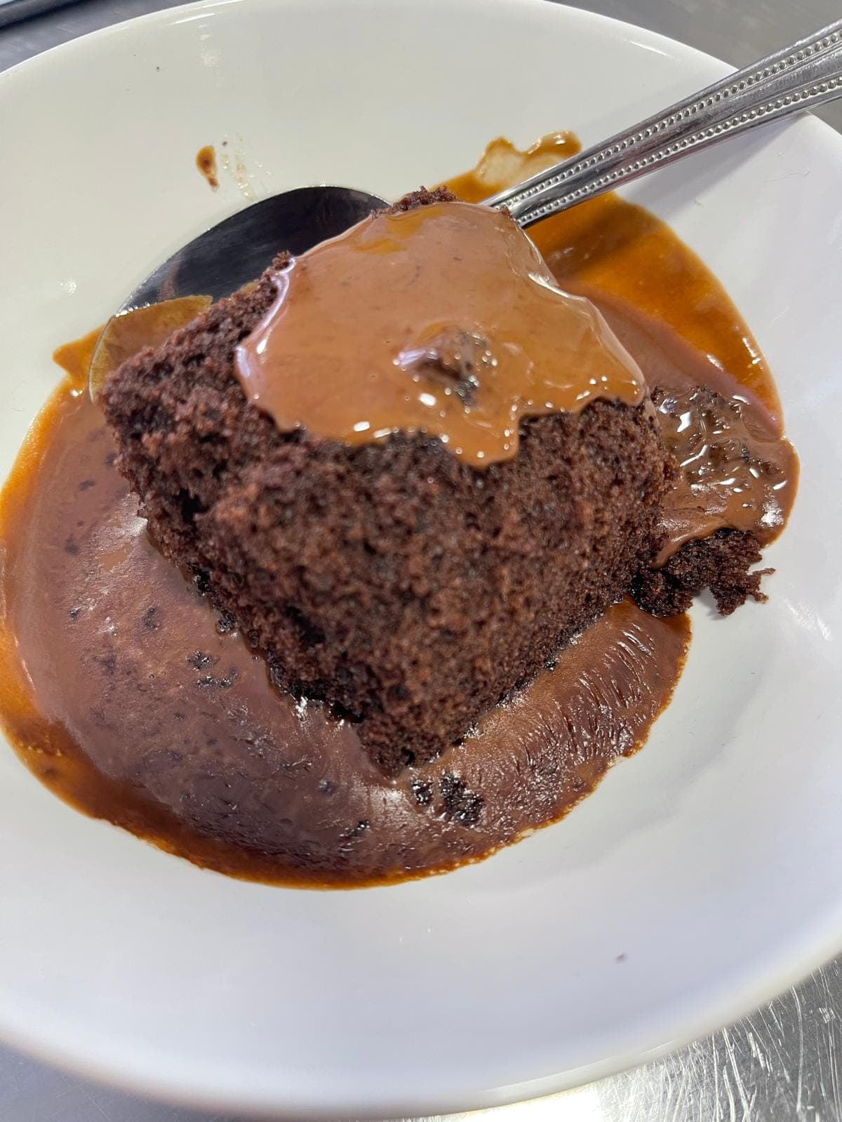 A warm chocolate sponge pudding in a bowl with chocolate sauce poured over it