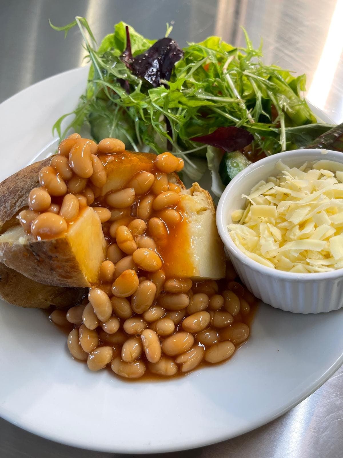 A jacket potato with baked beans, a pot of grated cheese and a side salad